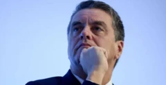 Imagem de Roberto Azevêdo usando terno, com a mão no queixo, foto tirada em ângulo inferior, sob um fundo azul claro
