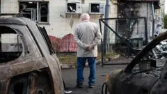 старий чоловік дивиться на зруйнований будинок