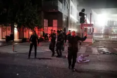 Pessoas na rua à noite em área com destroços; uma das pessoas sinaliza algo com as mãos