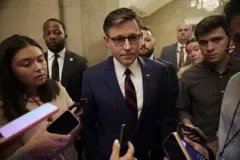 Mike Johnson usa óculos e está de terno e gravata em meio a vários jornalistas