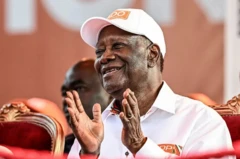 Alaasa Ouattara, assis avec une casquette et chemise blanche, applaudit tout souriant