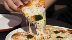 Mão levanta um pedaço de pizza, com queijo derretido sendo puxado