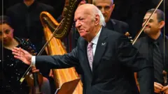 الموسيقار عمر خيرت في إحدى حفلاته يرتدي بذلة سوداء ويلقي التحية على الجمهور