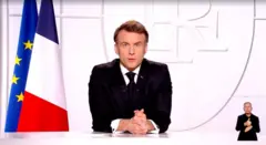 Macron sentado, falando e olhando em direção à TV