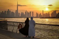 Casal olha para os arranha-céus de Dubai ao entardecer, em um passeio marítimo