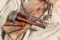 Alguns pregos, um martelo, uma coroa de espinhos sobre um pedaço de madeira manchado de sangue