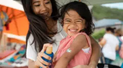 Ilustrasi seorang ibu mengolesi tabir surya di tangan anaknya