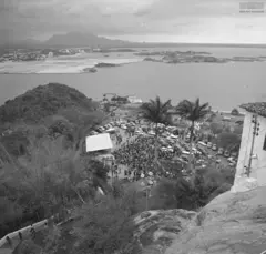 Foto preta e branca da vista do alto de uma pedra mostra o mar e uma cidade ao fundo