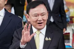 အနောက်တိုင်းဝတ်စုံအနက်ရောက်ကုတ်အင်္ကျီနဲ့ ထိုင်းဝန်ကြီးချုပ်ဟောင်း ဘီလျံနာသူဌေးကြီး သက်ဆင်ရှင်နာဝပ် လက်ပြနှုတ်ဆက်နေပုံ။ 