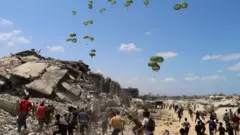 Palestinos correm em direção a paraquedas carregando pacotes de ajuda humanitária lançados de avião sobre o norte da Faixa de Gaza, em 7 de agosto de 2025