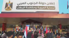 تابلوی بزرگی در بالای یک ساختمان که روی آن نوشته دولت جنوب عربی، مردم در مقابل ساختمان ایستاده‌اند