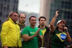 Jair Bolsonaro em um carro de som, ao lado dos filhos Carlos, Flavio e Jair Renan e da esposa Michelle, que discursa ao microfone. Todos usam as cores verde e/ou amarelo.