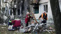 Robotnicy sprzątają gruz przed budynkiem mieszkalnym uszkodzonym podczas nocnego ataku rosyjskiego drona i rakiety w Kijowie, podczas rosyjskiego ataku na Ukrainę