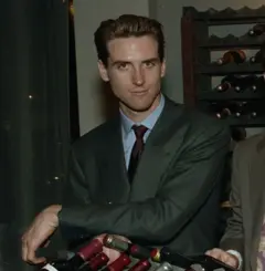Gavin Newsom jovem, usando terno, rodeado de garrafas de vinho