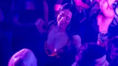 Cena de Anora mostra a protagonista dançando em boate