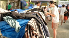 Uma mulher examina as roupas expostas nos painéis de avisos de uma rua movimentada.