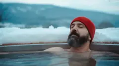 Homem com touca vermelha imerso em um ofurô no meio do gelo