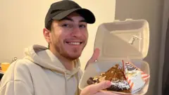 Jovem de boné sorrindo ao mostrar comida dentro de embalagem