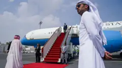 Из самолета по красной дорожке выходит мужчина в костюме, на первом плане его встречают два катарца в традиционной белой одежде.
