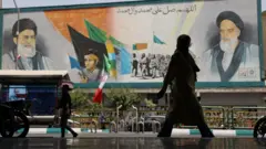 伊朗德黑蘭街頭一位女士走過歌頌最高領袖哈梅內伊的大型廣告（26/4/2025）