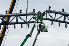 Trabajadores en grúas ensamblan partes metálicas que harán parte de la estructura de un arena temporal para peleas de artes marciales mixtas
