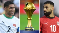 Photo montage avec Achraf Hakimi souriant, le trophée de la Coupe d'Afrique des Nations posé sur un socle bleu et Mohamed Salah. Hakimi porte un maillot blanc du Maroc floqué du numéro 2, tandis que Salah, vêtu d'un maillot rouge de l'Égypte portant le numéro 10. Au milieu de l'image, le trophée de la CAN.