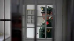 Um guarda visto por trás de grades de uma prisão