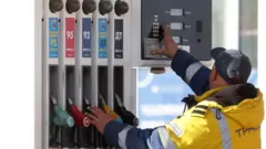 Сотрудник АЗС в Москве в желтой фирменной куртке со светоотражательными полосками стоит у кранов с бензином спиной к объективу