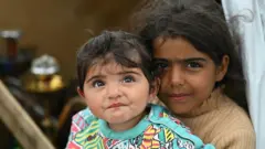 فتاة نازحة تحمل أختها عند مدخل خيمة في مخيم غير رسمي للنازحين في بيروت