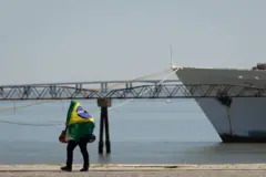 Pessoa andando com bandeira do Brasil nas costas, na beira do rio
