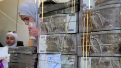 أكوام من الأوراق النقدية السورية في محل صرافة في دمشق، في 16 أبريل/نيسان 2025