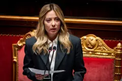 Meloni altın varaklı kırmızı bir koltuk önünde elinde bir kağıtla mikrofonda konuşuyor