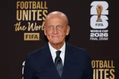 Pierluigi Collina, vestido de traje negro y corbata negra con una camisa blanca, está sentado en el Centro John F. Kennedy. Atrás tiene una pancarta que dice "Football Unites The World. FIFA World Cup 2026 Final Draw" y tiene una foto de la Copa del mundo
