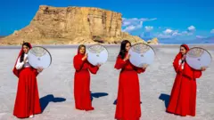 Cuatro mujeres iraníes con vestidos rojos y sosteniendo imágenes circulares realizan una actuación en el lecho seco del lago Urmia el 11 de abril de 2023, para llamar la atención sobre las crisis del cambio climático.
