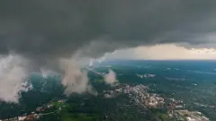 Vista aérea de uma cidade com abundantes áreas verdes e grupos de edifícios dispersos, coberta por nuvens escuras