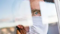 Homem de máscara olha pela janela