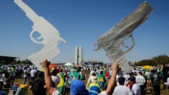 Un hombre muestra dos carteles con forma de revólver durante una manifestación pro/armas en apoyo a Bolsonaro en Brasilia.