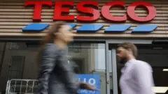 Two people walk past a Tesco store