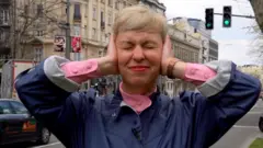 BBC novinarka na ulici Beograda prikriva uši rukama