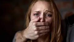 Una hombre tapa la boca de una mujer con la mano.