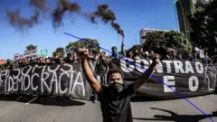 Jovem ajoelhado diante de faixas em manifestação