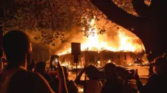 People look on as a construction site burns in a large fire near the Third Police Precinct