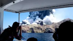 Turistas viendo y fotografiando desde un bote el volcán en plena erupción.
