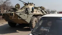 A refugee waits in a car as an armoured personnel carrier of pro-Russian troops drives out of a checkpoint in the besieged city of Mariupol