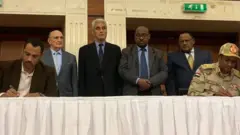 Umukuru w'abatavuga rumwe n'ubutegetsi (ibumoso) n'uwungirije umukuru w'inama ya gisirikare (iburyo) bashyira umukono ku masezerano, imbere y'abahuza