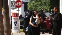 Mujer con chico en brazos y agentes de policía detrás