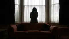 One young woman wey dey suffer from domestic violence for Asia stand near window for her house