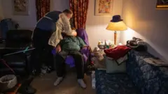 Un ambulancier portant un équipement de protection individuelle (EPI), met un masque chirurgical à un patient afro-américain présentant les symptômes du COVID-19 dans son appartement.