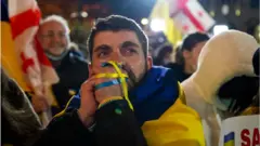 Učastnik akcii v Tbilisi slušaet vыstuplenie Vladimira Zelenskogo