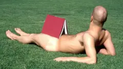 Nackter Mann mit Buch im Gras liegend